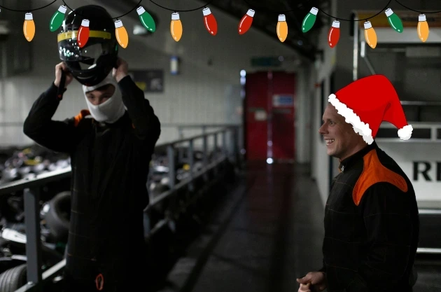 Two people getting ready to race on a go karting track. One person is putting on a helmet.